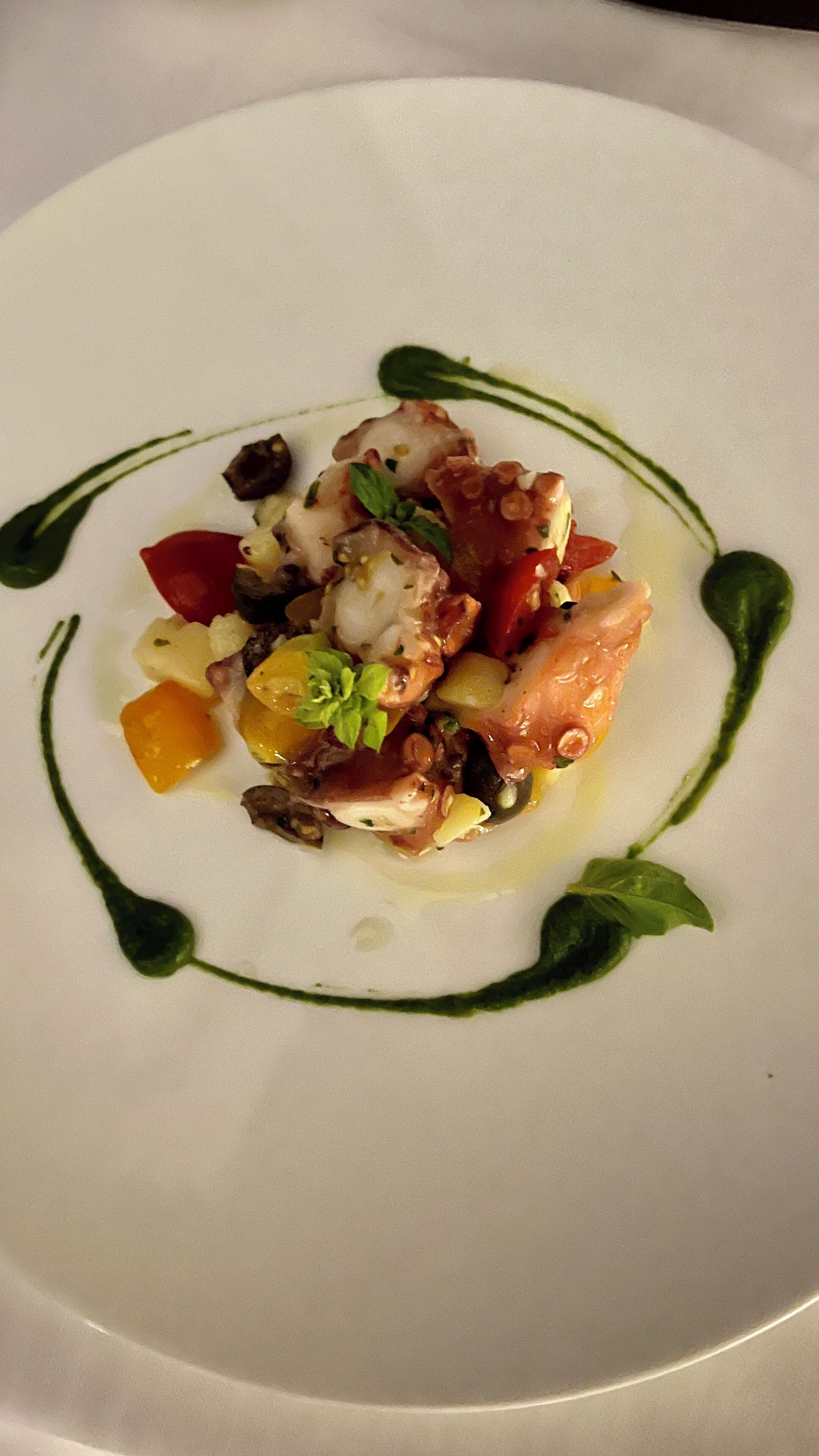 A white plate with a seafood dish, garnished with herbs and surrounded by a green sauce.