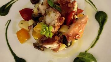 A white plate with a seafood dish, garnished with herbs and surrounded by a green sauce.