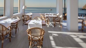 A restaurant with tables and wicker chairs, overlooking a body of water. - Apollon Club (Serrara Fontana)