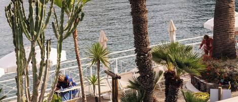 A swimming pool with a view of a coastal area, including a rocky cliff and a building with balconies.