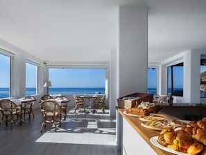 A spacious dining area with a view of the sea, featuring wicker chairs, a wooden table, and a buffet with pastries and bread. - Apollon Club (Serrara Fontana)