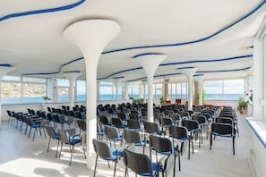 Een vergaderzaal met rijen stoelen, grote ramen en uitzicht op zee.