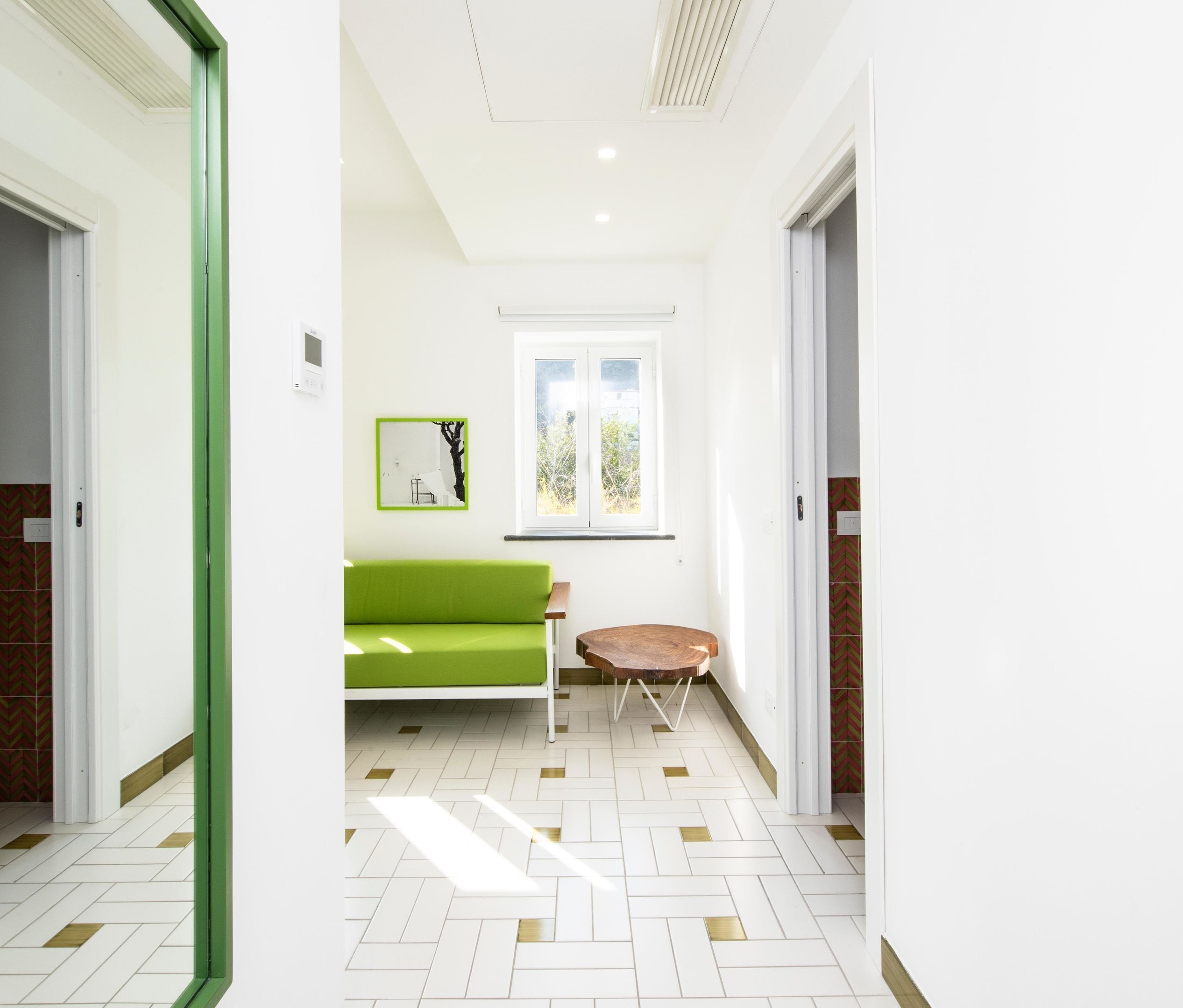 A hallway with a green sofa, a small round table, and a window with a view of greenery.