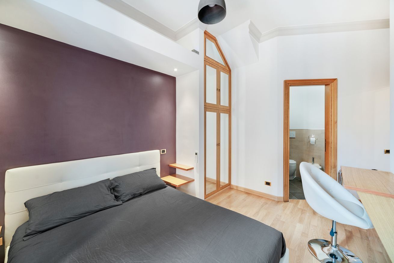 A bedroom with a large bed, a wooden door, a mirror, and a small bathroom.