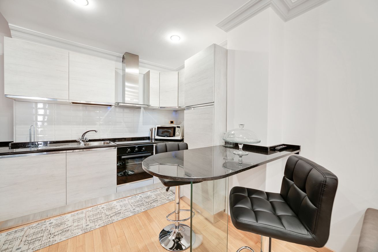 A modern kitchen with white cabinetry, a round glass table, and a black leather chair.