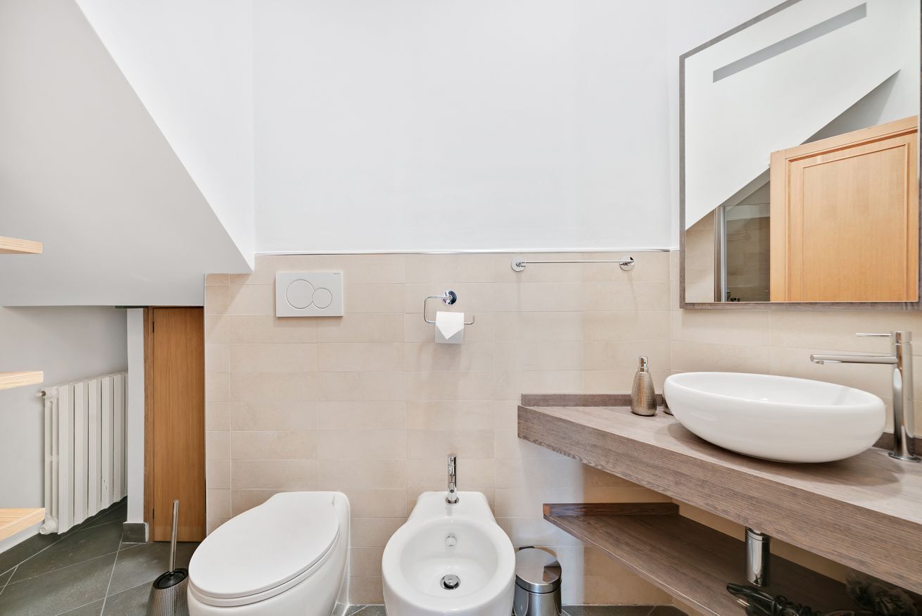 A modern bathroom with a toilet, bidet, and a large sink on a wooden countertop.