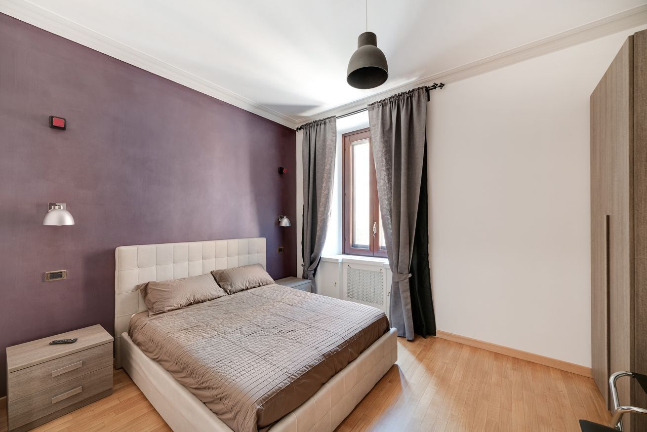 A bedroom with a bed, bedside tables, a window with curtains, and a hanging light fixture.