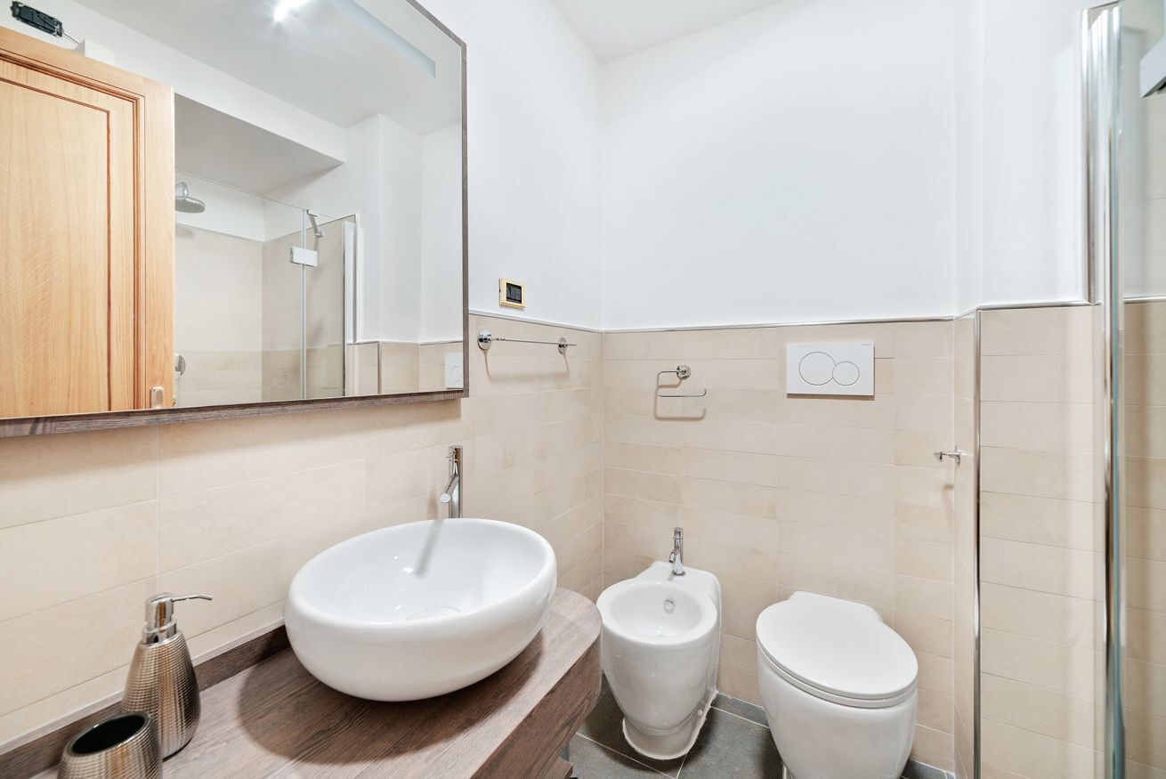A modern bathroom with a large mirror, a vessel sink, a bidet, and a toilet.