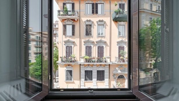 Uitzicht door een raam op een gebouw met meerdere balkons, grote ramen en een klassieke architectuur.