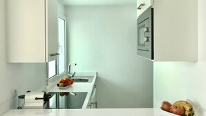 A modern kitchen with white cabinetry, a stainless steel sink, and a fruit bowl on the counter. - Casa Atlantica - beautiful Seaview Apartment (Las Playitas)