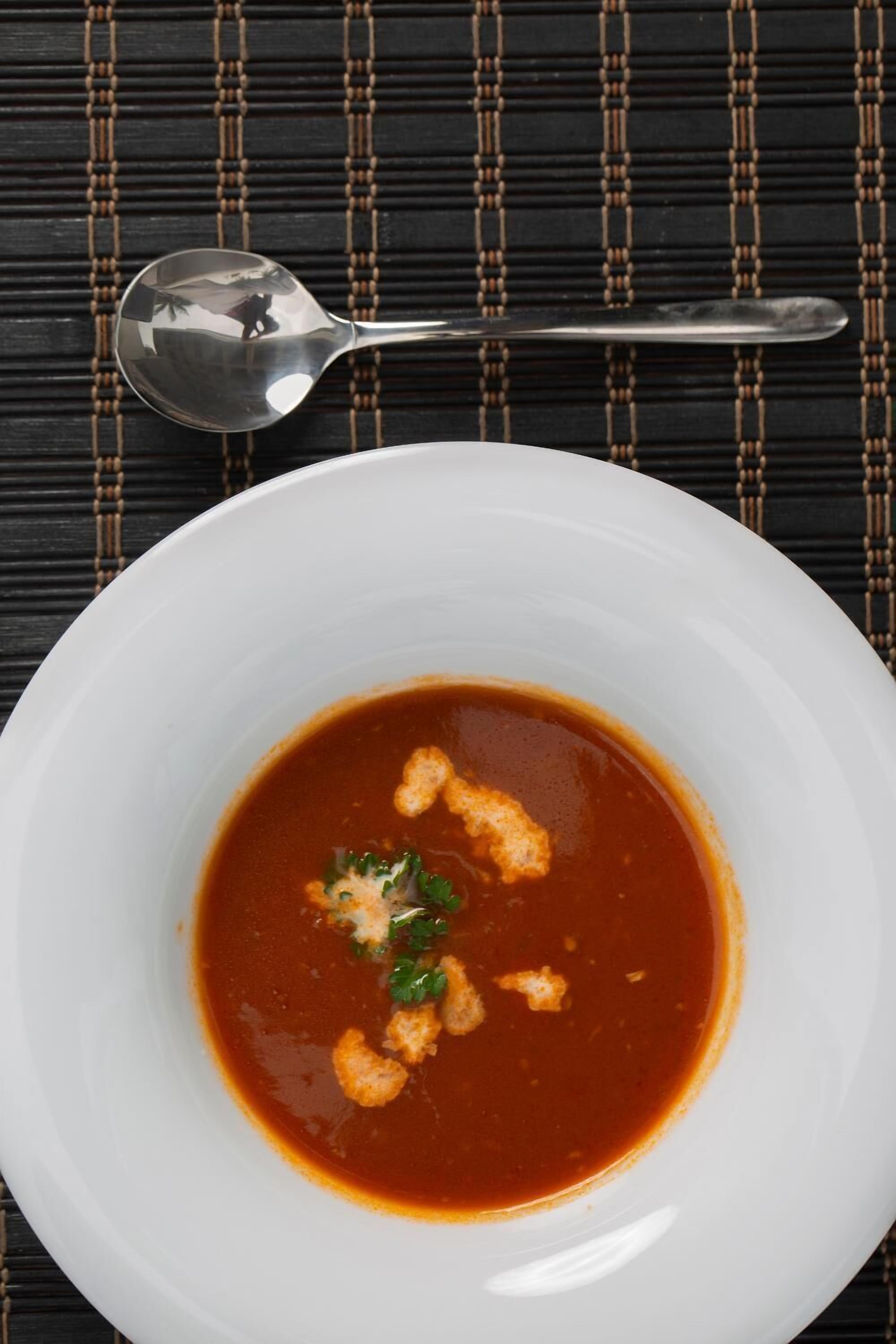 Un bol blanc de soupe, avec une cuillère, posé sur un tapis tissé de couleur sombre.