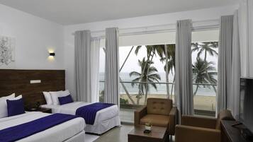 Habitación de hotel con dos camas, un sofá, un televisor y vista a la playa.