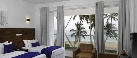 Habitación de hotel con dos camas, un sofá, un televisor y vista a la playa.