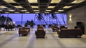 A spacious lounge area with multiple sofas and chairs, a flat-screen TV, and a view of the ocean and palm trees.