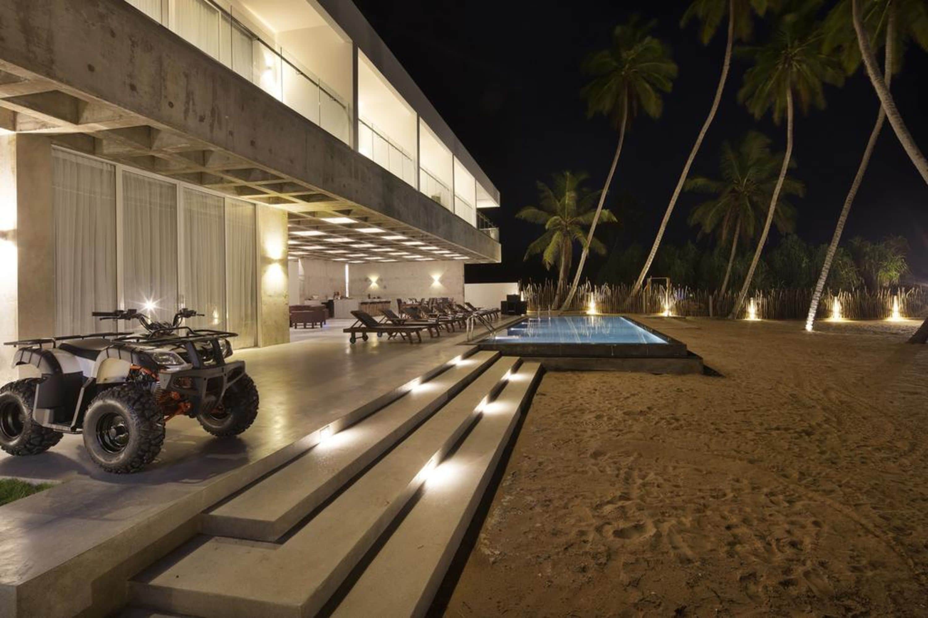 Un bâtiment moderne doté d’une piscine et d’un espace extérieur aménagé pour se détendre, le tout illuminé la nuit.