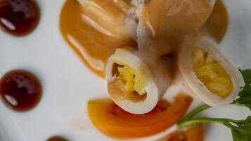 Primer plano de un plato con rollitos rellenos de un relleno amarillo, acompañados de salsa oscura y rodajas de naranja.