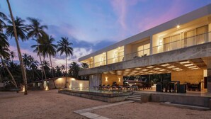 A modern two-story building with a swimming pool and outdoor seating area, surrounded by palm trees.