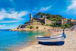 Une plage avec un bateau, une eau d’un bleu cristallin et un fort historique perché sur une colline.