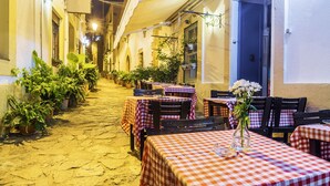 A narrow cobblestone street lined with outdoor tables and chairs, each covered with a checkered tablecloth.