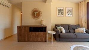 A modern living room with a wooden cabinet, a round mirror, a grey sofa with cushions, and two framed artworks on the wall.