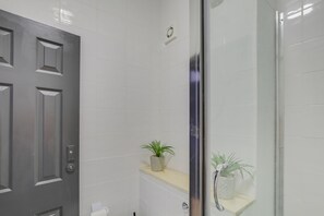 Bathroom features a glass shower enclosure, toilet, and sink, with a potted plant adding a touch of greenery.