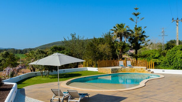 Une piscine avec une terrasse en bois, des chaises longues et un parasol.