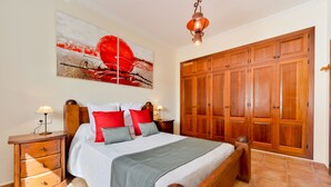 Une chambre avec un grand lit, une armoire en bois et un tableau accroché au mur.