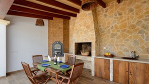 Un espace extérieur aménagé pour les repas, avec une cheminée en pierre, une table et des chaises en bois, et un mur en pierre.