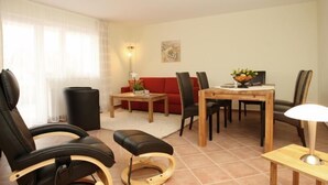 Un salon moderne avec un canapé rouge, des fauteuils en cuir noir, une table à manger en bois et une petite table d’appoint avec une lampe.