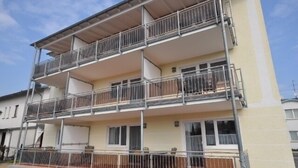 Un immeuble résidentiel de trois étages, doté de balcons, d’une entrée couverte et d’une porte de garage visible.