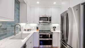 A modern kitchen with white cabinets, a stainless steel refrigerator, a microwave, and an oven.