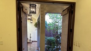 A hallway with a tiled floor leading to an outdoor area with a wooden fence and a tree.