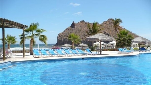 A swimming pool with blue lounge chairs and a mountain in the background.