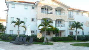 Un hotel de varios pisos con balcones, palmeras y sillones de descanso.