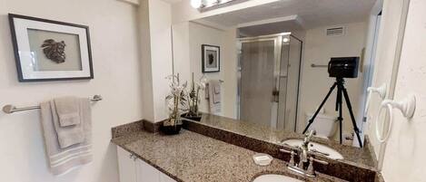 A bathroom with a granite countertop, two sinks, a large mirror, and a camera on a tripod.