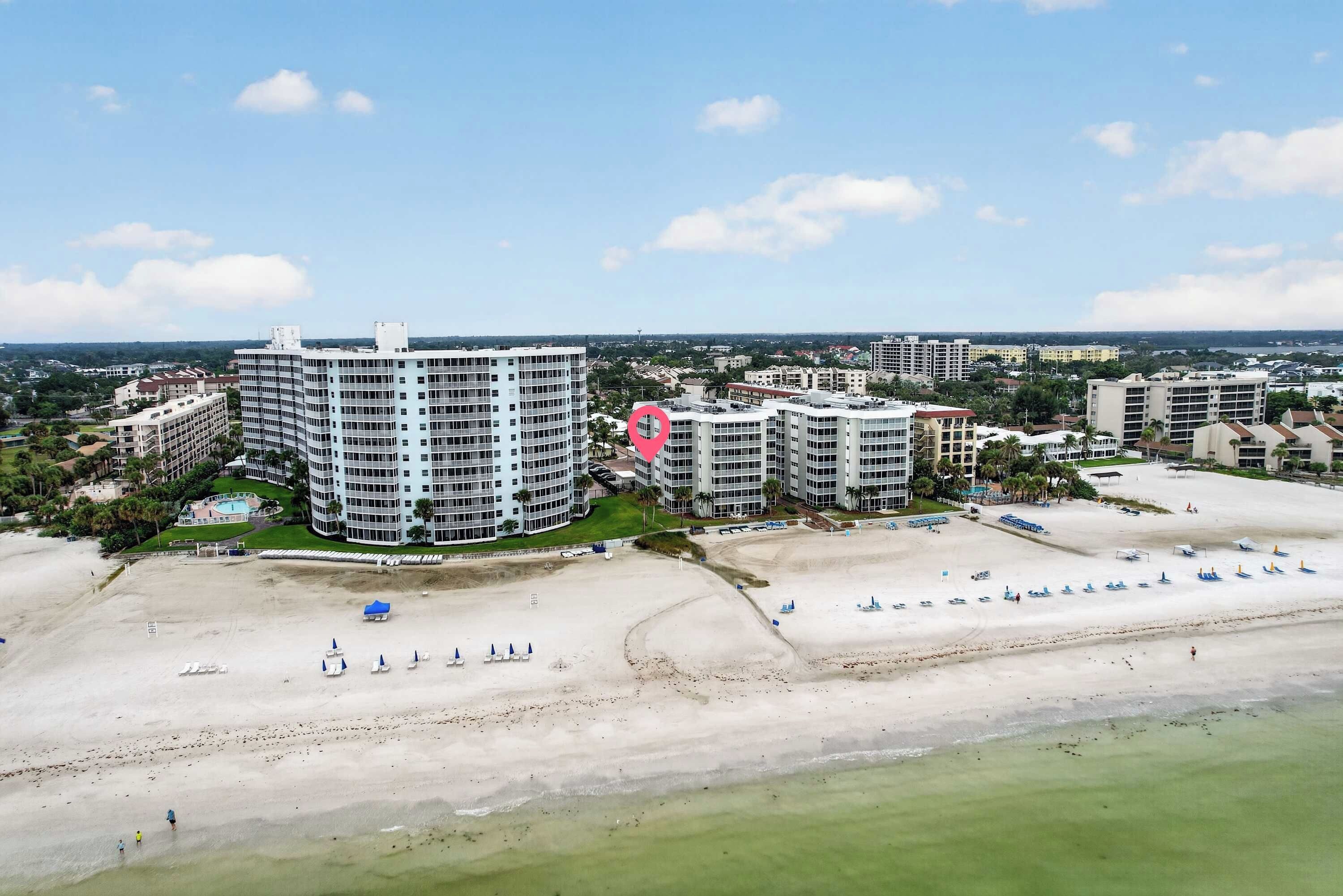 A coastal resort area with beachfront properties, including a large hotel with multiple floors and balconies, and a smaller building nearby.