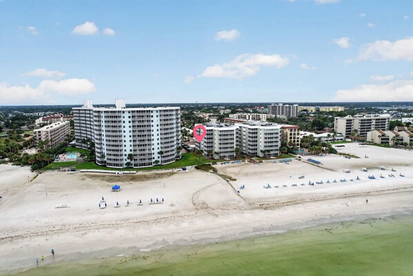 A coastal resort area with beachfront properties, including a large hotel with multiple floors and balconies, and a smaller building nearby. - Beach & Pool Open! Beachfront View Every Room (Siesta Key)