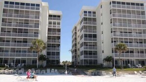 A beachfront hotel with multiple floors, balconies, and a sandy beach area with sun loungers. - Beach & Pool Open! Beachfront View Every Room (Siesta Key)