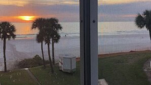 A view through a window with a sunset, palm trees, and a white building. - Beach & Pool Open! Beachfront View Every Room (Siesta Key)