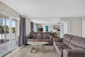 A modern living room with two grey sofas, a small round coffee table, and a view of the outside balcony. - Beachfront Unit! Gulf View from Every Room. Lanai (Siesta Key)
