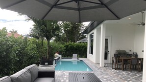 Zona de piscina con área de estar techada, una parrilla y una mesa de comedor.
