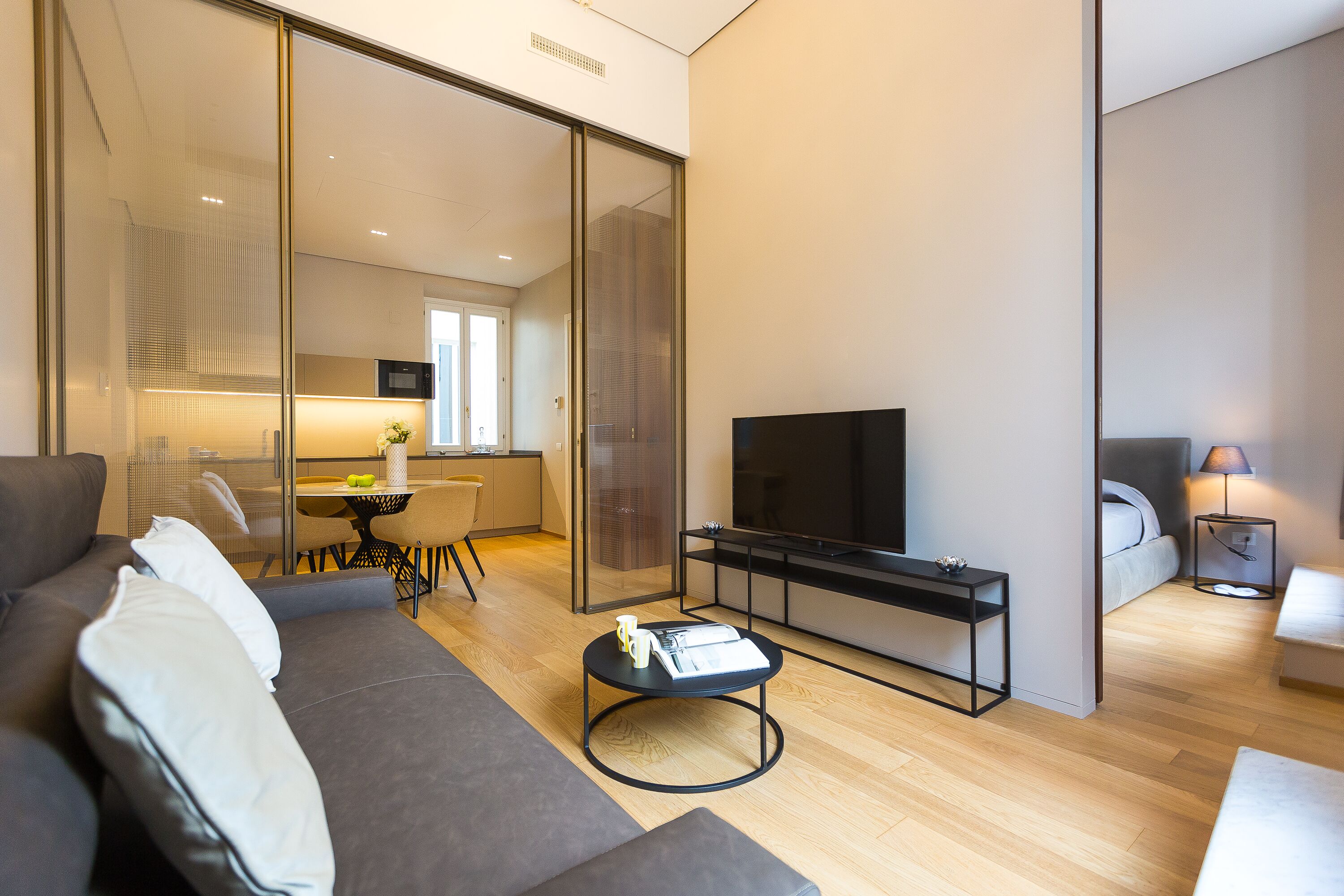 A modern living room with a sofa, a coffee table, a TV, and a dining area with a table and chairs.