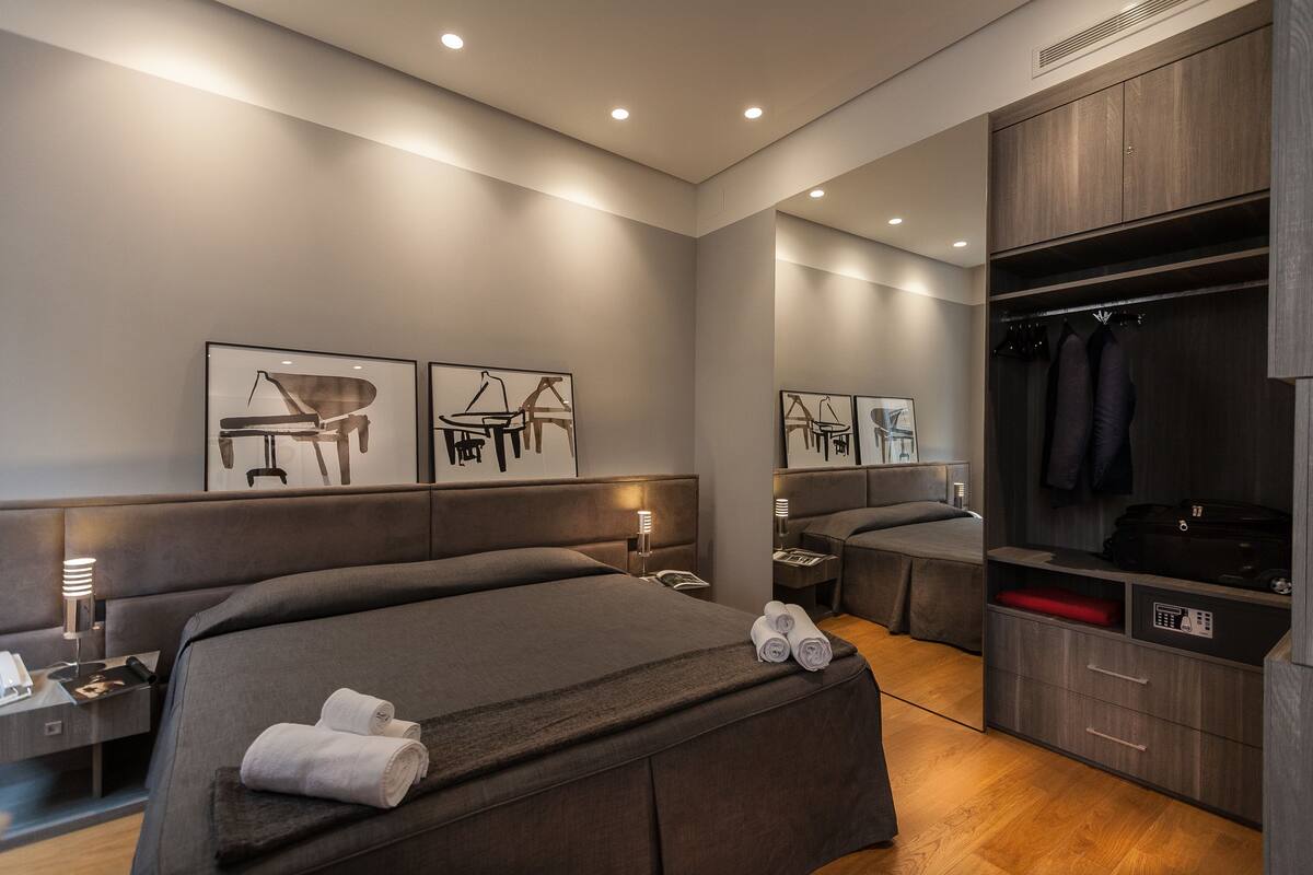 A modern hotel room with a large bed, a desk, a wardrobe, and artwork on the walls.