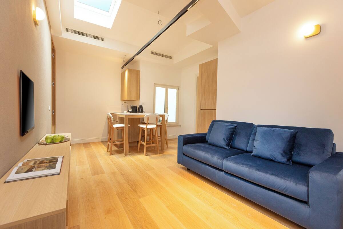 A modern living room with a blue sofa, wooden dining table, and chairs.