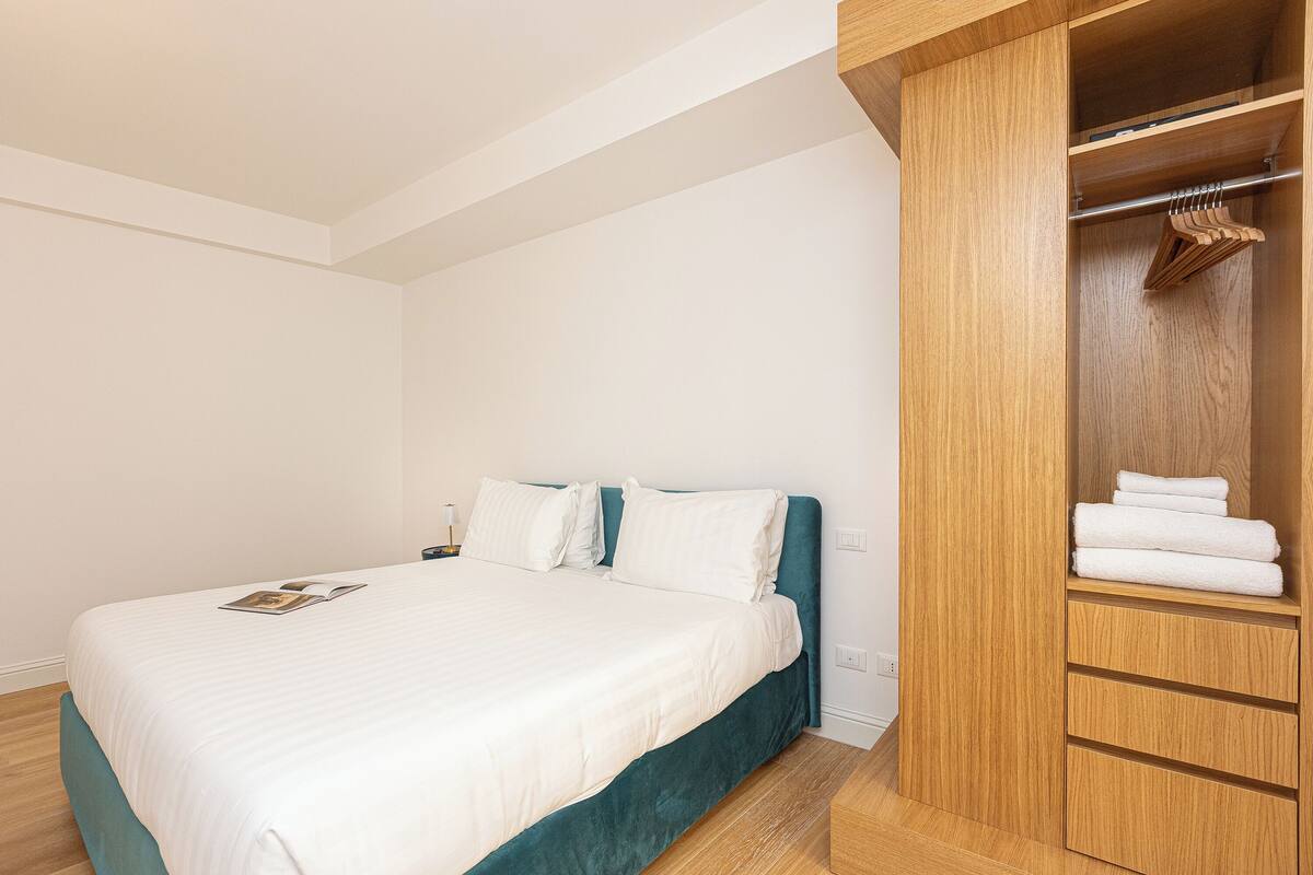 A bedroom with a bed, a wooden wardrobe, and a nightstand.