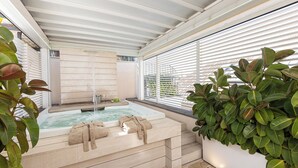 Een wellnessruimte met een jacuzzi, handdoeken en een grote plant in pot.