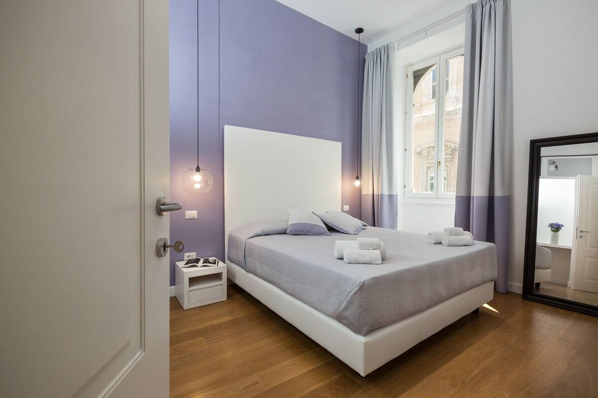 A modern bedroom with a large bed, bedside tables, and a window with curtains.