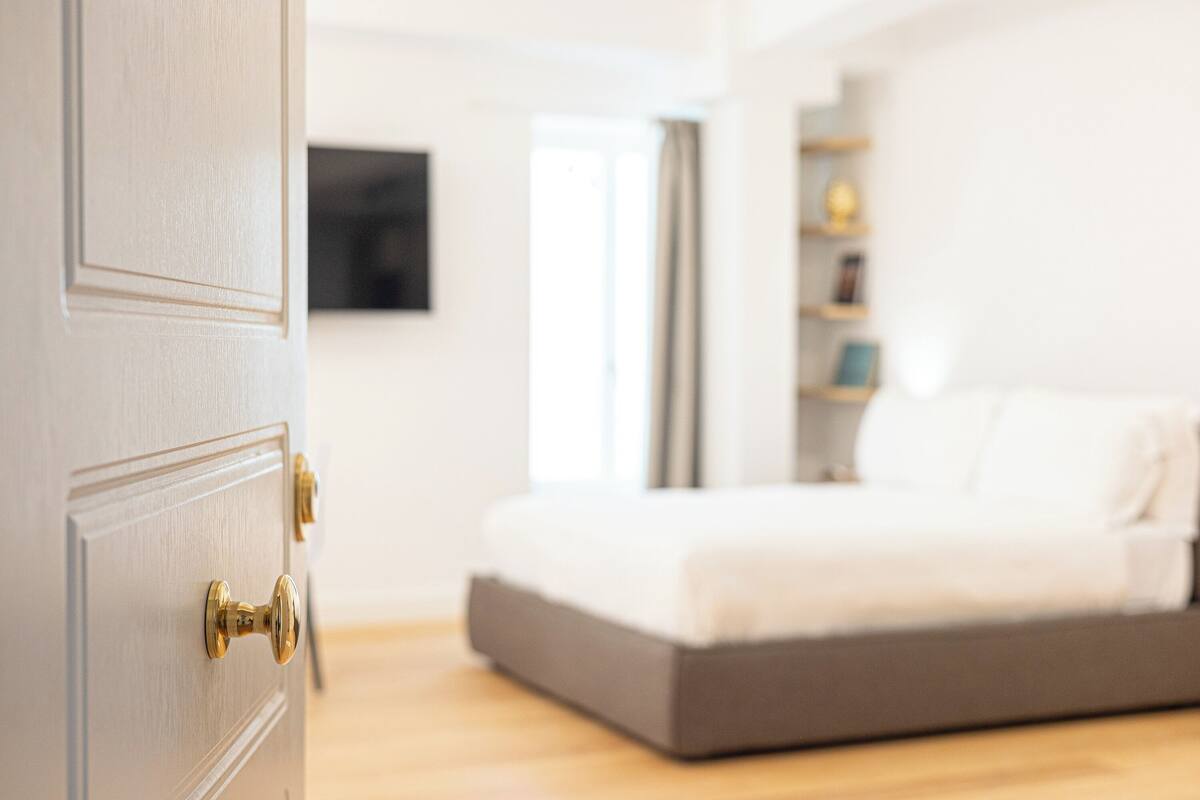 A bedroom with a bed, a door with a brass handle, and a bedside table.