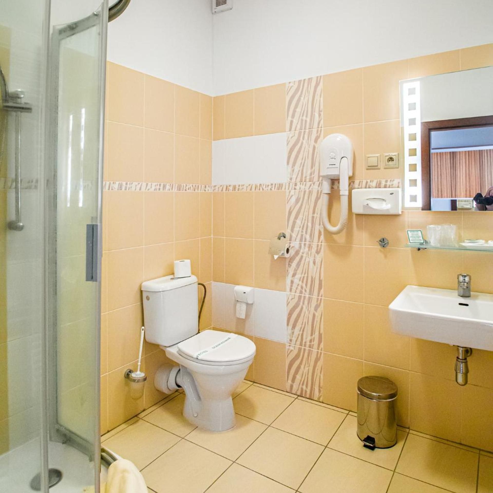 A bathroom with a toilet, a shower, a sink, and a trash bin.