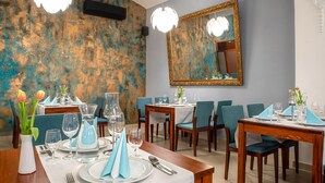 A dining area with tables set for two, blue napkins, and tulips in vases. - Hotel Academic (Zvolen)